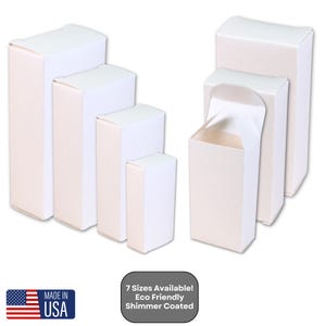 Puede incluir: Siete tamaños de cajas de cartón blanco con un acabado brillante. Las cajas están dispuestas en una fila de la más grande a la más pequeña. Las cajas están hechas de materiales ecológicos.  7 Tamaños Disponibles! Eco Friendly Shimmer Coated