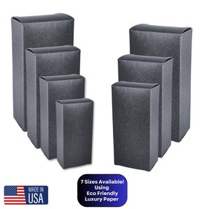 May include: Seven sizes of black cardboard boxes with a textured finish. The boxes are stacked in decreasing size from left to right. The text "7 Sizes Available! Using Eco Friendly Luxury Paper" is printed below the boxes.