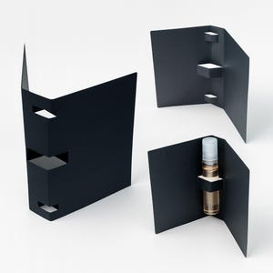 May include: Black cardboard packaging with cut-out details. One package holds a small glass vial with a light-colored liquid and a white and gray cap. The other packages are empty.