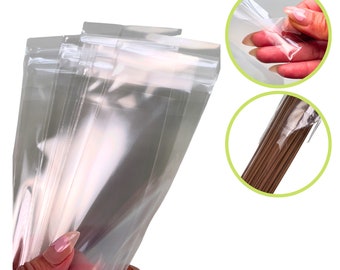 Puede incluir: Un montón de bolsas de plástico transparentes con cierres de cremallera resellables. Las bolsas están diseñadas para contener varillas de incienso. La imagen muestra un primer plano de las bolsas y una mano sosteniendo una de las bolsas.
