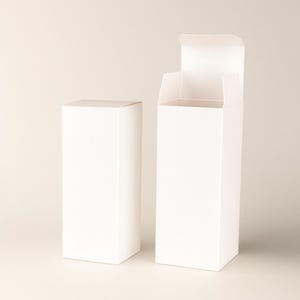 May include: Two white rectangular product boxes, one closed and one open. The open box has its top flaps extended, revealing the interior. Both boxes are made of a smooth, matte material and stand upright against a neutral background.