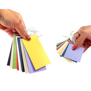 May include: A collection of colorful paper tags with string attached. The tags are in various shades of green, pink, red, blue, yellow, and purple.