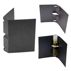 May include: Three views of a black, textured cardboard packaging. One view shows the packaging folded, with cut-out sections. Another view displays the packaging with a small glass vial containing a yellow liquid. The vial is held in place by a small cardboard insert.