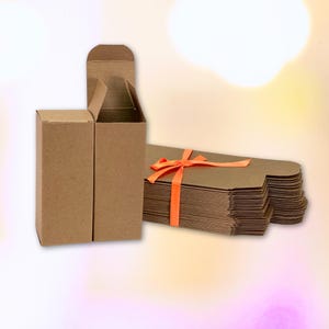 Puede incluir: Una pila de cajas de cartón marrón con una cinta naranja brillante atada alrededor. Dos cajas están de pie, una con la parte superior abierta.