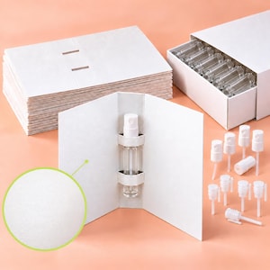 May include: A set of white cardboard display cards with die-cut slots for holding small clear glass spray vials. The set includes a stack of flat cards, a box filled with empty glass vials, and a collection of white plastic spray pump caps.