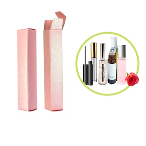 May include: Two pink cardboard boxes with glitter, one open and one closed, next to a circle containing five different bottles of beauty products, including a mascara, a clear serum, a rollerball bottle, and two clear bottles with pink and green liquid.