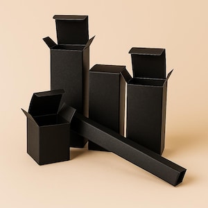 May include: A collection of black cardboard boxes in different sizes, set against a neutral backdrop. Some boxes are open, displaying their interiors, while others are closed. The boxes are rectangular with a matte finish.