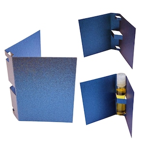 May include: Three blue sample card holders with a textured finish. One holder is folded and empty, another has cut-out slots, and the third holds a small glass vial with a clear cap and yellow liquid.