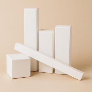 Könnte beinhalten: Eine Ansammlung weißer Produktboxen in verschiedenen Formen und Größen. Dazu gehören ein Würfel, rechteckige Boxen und eine lange, schlanke Box. Die Boxen sind auf einem neutralen Hintergrund angeordnet, was eine saubere und minimalistische Ästhetik erzeugt.
