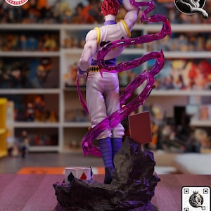 Puede incluir: Figura detallada de un personaje con cabello rojo, vistiendo un atuendo blanco y morado, y sosteniendo un arma. La figura est&aacute; posada din&aacute;micamente con un efecto de energ&iacute;a p&uacute;rpura transl&uacute;cida. Un peque&ntilde;o libro y un cubo con s&iacute;mbolos de cartas est&aacute;n en la base.
