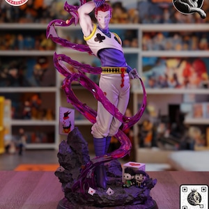 Puede incluir: Figura detallada de un personaje en pose din&aacute;mica, sosteniendo naipes y un objeto morado en forma de cinta. La figura viste un atuendo blanco y morado con un s&iacute;mbolo de tr&eacute;bol negro. La base presenta peque&ntilde;as figuras y naipes.