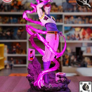 Puede incluir: Figura detallada de un personaje en pose din&aacute;mica, sosteniendo una carta de juego. La figura viste un atuendo blanco y morado con detalles en rosa, y est&aacute; rodeada de efectos de energ&iacute;a rosa brillante. La base incluye figuras adicionales.
