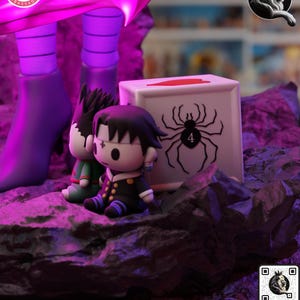 Puede incluir: Una vibrante exhibici&oacute;n de figuras estilizadas con dos figuras de estilo anime y una caja blanca con un gr&aacute;fico de ara&ntilde;a. Las figuras est&aacute;n sobre una base rocosa iluminada en p&uacute;rpura. La caja tiene una parte superior roja y el n&uacute;mero 4.