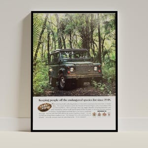 Puede incluir: Impresión enmarcada de un Land Rover Defender 90 Wagon vintage en un bosque. El vehículo verde oscuro es el foco, con el texto "Keeping people off the endangered species list since 1948." en la parte superior. Marco negro.