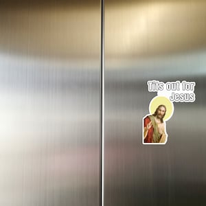 May include: A white sticker with the text "Tits out for Jesus" and a picture of Jesus Christ.