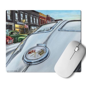 May include: Mousepad featuring a painting of a classic white car with a chrome emblem and checkered flags. The background shows a street scene with vintage cars and buildings. A white computer mouse is next to the mousepad.