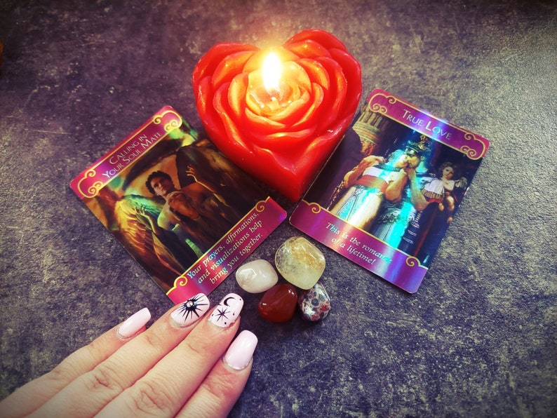 May include: Two oracle cards with a red heart-shaped candle, crystals, and a hand with pink and white nail polish. The cards are "Calling in Your Soul Mate" and "True Love". The text on the cards reads "Your prayers, affirmations, and visualisations help bring you together." and "This is the romance of a lifetime!"