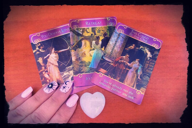 May include: Three oracle cards with colourful illustrations and text. The cards are laid out on a wooden surface. The text on the cards reads "You Deserve Love", "Retreat", and "This Could Be The One".