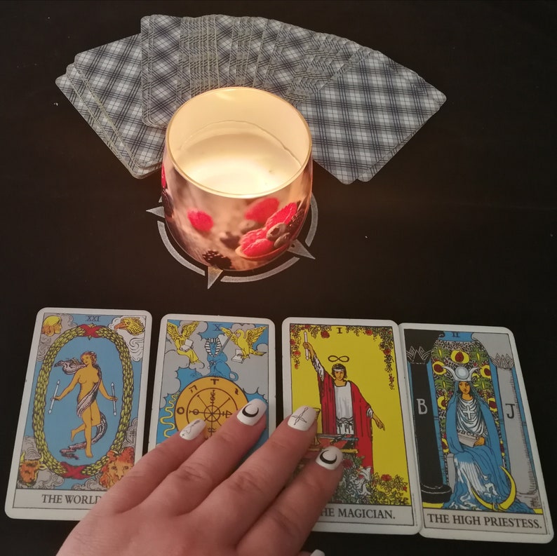 May include: Tarot card reading with a lit candle and a hand holding the cards. The cards are "The World", "The Magician", and "The High Priestess".