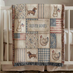 May include: A patchwork baby blanket with a cream background and various squares featuring bunnies, dachshunds, chickens, and American flags. The blanket has the name "OLIVER JAMES" in the center and a fringed edge.