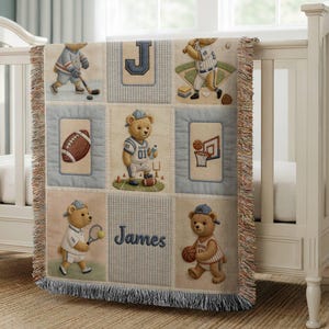 Peut inclure: Une couverture pour bébé avec un motif patchwork représentant des ours en peluche sur le thème du sport. La couverture comprend des images de hockey, de baseball, de football, de basket-ball et de tennis. Le nom "James" est brodé sur la couverture.