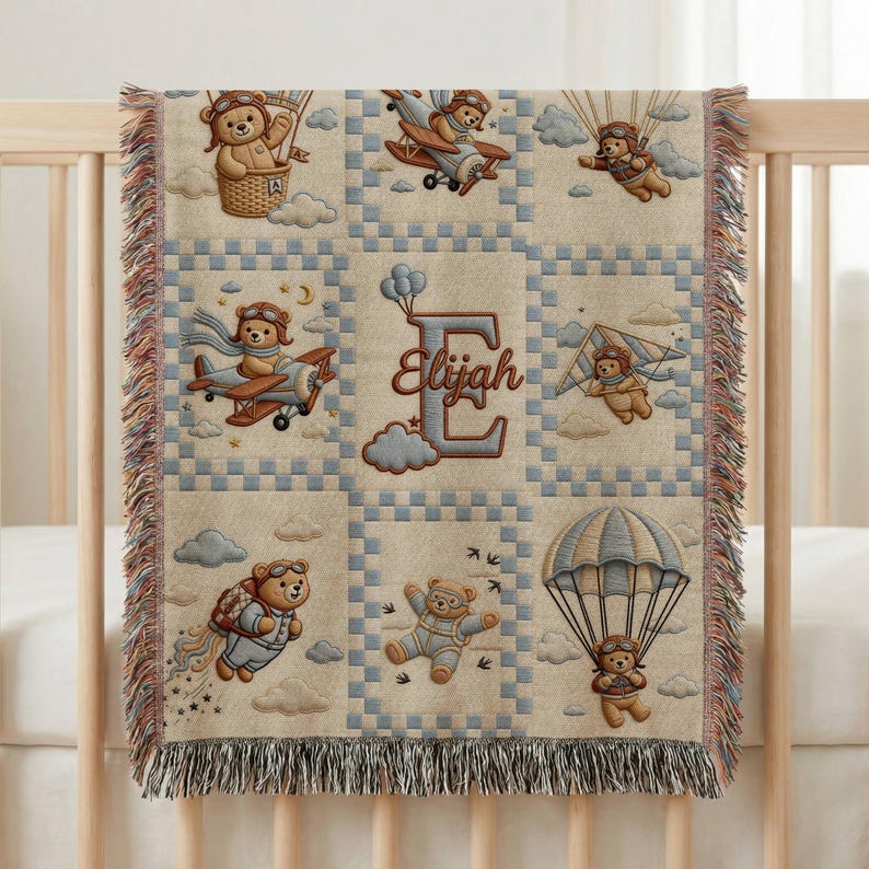 May include: A woven throw blanket featuring a grid pattern with illustrations of teddy bears in aviation gear, including hot air balloons, airplanes, and parachutes. The center block displays a large letter E with the name Elijah in script.