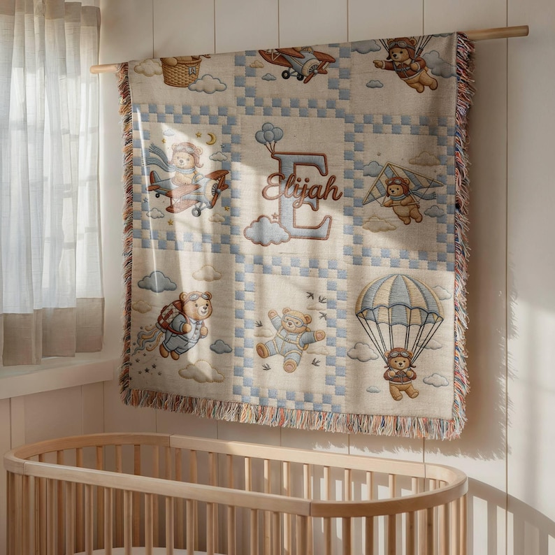 May include: A woven throw blanket featuring a grid pattern with illustrations of teddy bears flying in airplanes, hang gliders, and parachutes. The center panel displays a large letter E with the name Elijah written in cursive script.