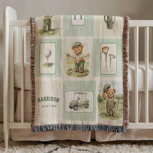 May include: A beige baby blanket with a golf theme. It features illustrations of a golf ball, golf clubs, a golf cart, and a teddy bear golfer. The blanket has a striped pattern and the name "Harrison" and date "June 26th, 2026" printed on it.