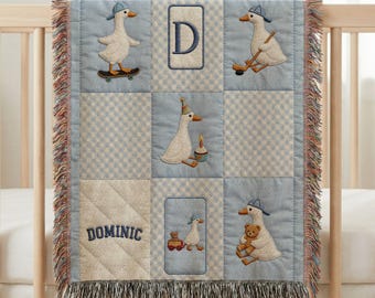 May include: A baby blanket with a light blue and white checkered pattern, featuring embroidered images of a goose wearing a hat and playing sports. The blanket has a fringed edge and the name "Dominic" is embroidered on it.