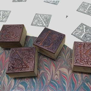 May include: Four wooden printing blocks with intricate floral designs and letters carved into them. The blocks are arranged on a marbled surface.