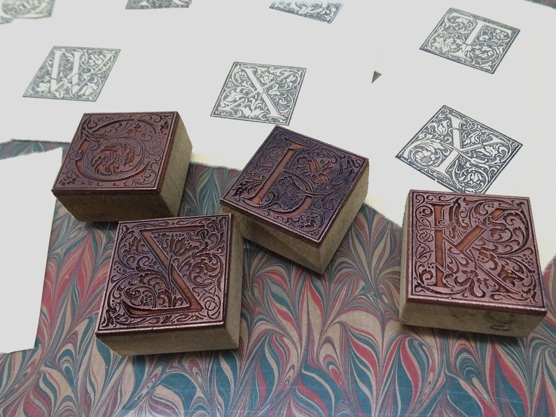 May include: Four wooden printing blocks with intricate floral designs and letters carved into them. The blocks are arranged on a marbled surface.