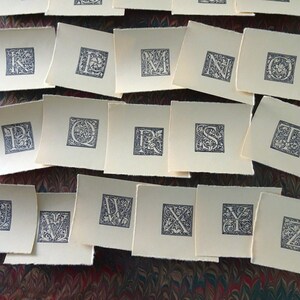May include: A set of 26 alphabet letter cards with decorative floral designs in black ink on white paper.