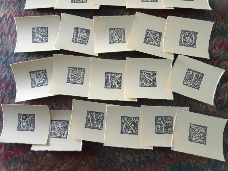 May include: A set of 26 alphabet letter cards with decorative floral designs in black ink on white paper.