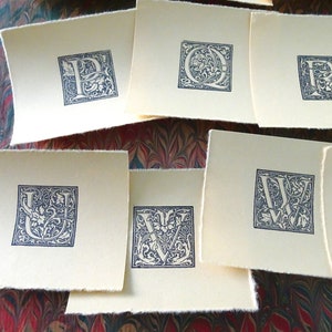 May include: A set of nine cream-colored cards with black ink, each featuring a different letter of the alphabet in a decorative, ornate font.