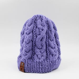 May include: A purple knitted beanie with a cable knit pattern. The beanie has a small brown leather tag with the text "Made with Love" on it.