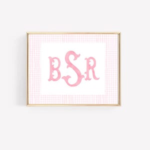 May include: A framed print featuring a pink monogram with the letters BSR in a decorative font. The monogram is set against a white background with a pink gingham border, all within a gold-colored frame.