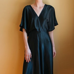 Può includere: Una donna indossa un abito avvolgente in raso nero con scollo a V e maniche corte.