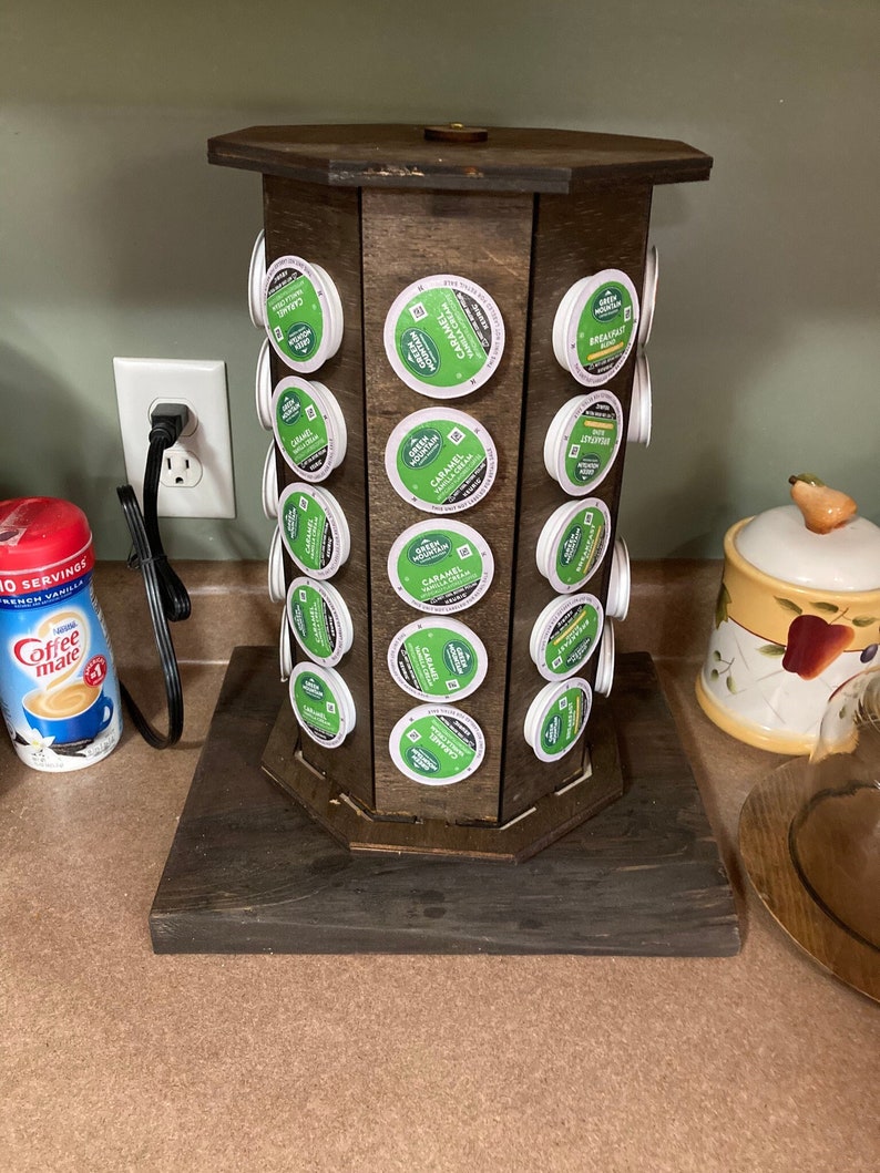 May include: A wooden coffee pod holder with a rotating carousel. The holder is filled with single-serve coffee pods in various flavors, including Green Mountain Coffee Roasters Caramel Vanilla Cream and Green Mountain Coffee Roasters Breakfast Blend.