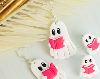 May include: White ghost earrings with black eyes and a pink book. The earrings are made of a lightweight material and have silver hooks. The earrings are a fun, spooky accessory.