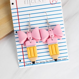 May include: Pink bow earrings with a yellow pencil charm. The earrings are on a white card with blue lines and the text "Thank you for being the best teacher ever!"