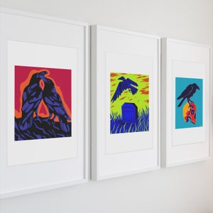Op de afbeelding: Drie ingelijste kunstprints in witte lijsten. De eerste print toont twee donkerblauwe raven tegen een rode en oranje achtergrond. De tweede toont een raaf die over een grafsteen in een groen veld vliegt. De derde toont een raaf op een schedel.