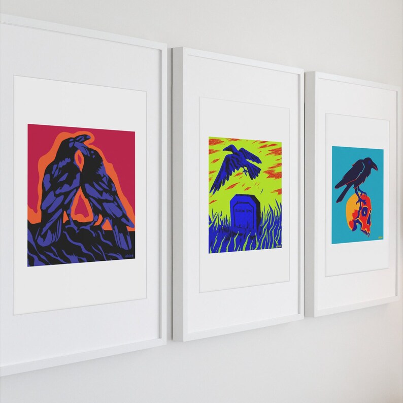 Op de afbeelding: Drie ingelijste kunstprints in witte lijsten. De eerste print toont twee donkerblauwe raven tegen een rode en oranje achtergrond. De tweede toont een raaf die over een grafsteen in een groen veld vliegt. De derde toont een raaf op een schedel.