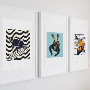 May include: Three framed illustrations of people engaged in water sports. The first shows a person surfing on a wave, the second shows a person scuba diving, and the third shows a person kayaking.