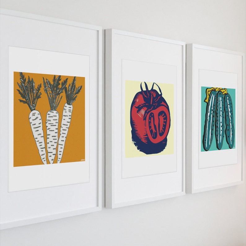May include: Three framed prints with colorful illustrations of vegetables. The first print features three white carrots with green tops on a yellow background. The second print features a red tomato with a green stem on a white background. The third print features three green cucumbers with yellow tops on a white background.