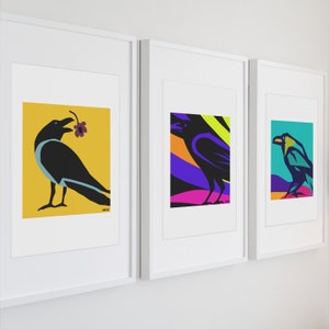 Op de afbeelding: Drie ingelijste kunstprints met gestileerde zwarte raven. De eerste print toont een raaf met een paarse bloem op een gele achtergrond. De tweede toont een raaf tegen abstracte paarse, oranje en groene vormen. De derde toont een raaf op een groenblauwe achtergrond.