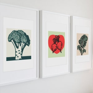 Könnte beinhalten: Drei gerahmte Drucke mit Illustrationen von Gemüse. Der erste Druck zeigt einen grünen Brokkoli, der zweite Druck zeigt zwei rote Rüben in Herzform und der dritte Druck zeigt ein grünes Blattgemüse.