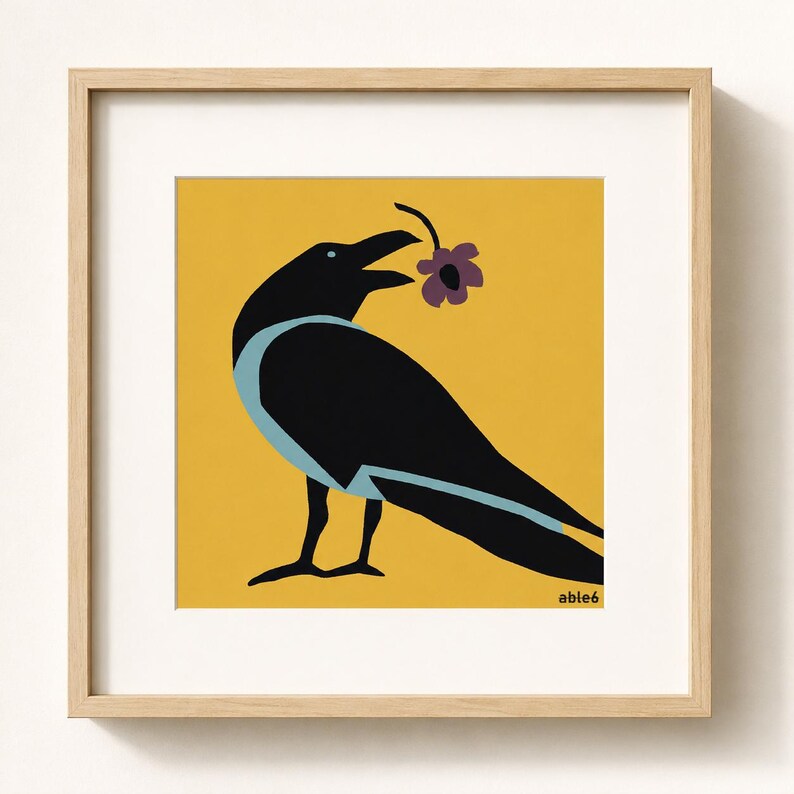 Op de afbeelding: Een ingelijste vierkante print met een zwarte kraai met lichtblauwe accenten op een mosterdgele achtergrond. De kraai houdt een kleine paarse bloem in de snavel. De tekst "able6" staat in het zwart in de rechterbenedenhoek van het kunstwerk.