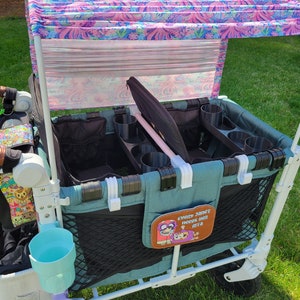 May include: A teal wagon with a black mesh storage area and a pink and white floral canopy. The wagon has multiple cup holders and a patch that says "Every Janet needs her ETA".