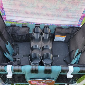 May include: A teal wagon with a black and teal fabric interior. The wagon has two seats with safety harnesses and a built-in cup holder with four slots.
