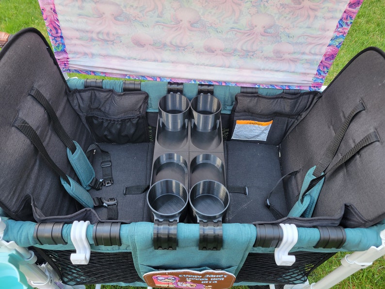 May include: A teal wagon with a black and teal fabric interior. The wagon has two seats with safety harnesses and a built-in cup holder with four slots.